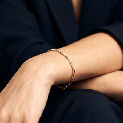 Gold chain bracelet on a wrist resting on crossed arms, black blazer
