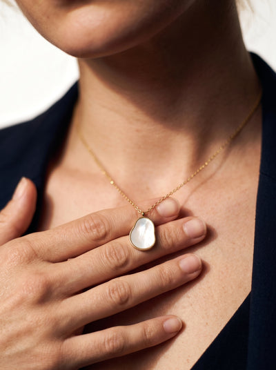 Mother-of-pearl pendant necklace, close-up with her hand resting on her chest