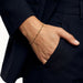 Anchor Twist Chain Bracelet – worn on the wrist, hand in the trouser pocket, gold, dark blazer, ivory studio background