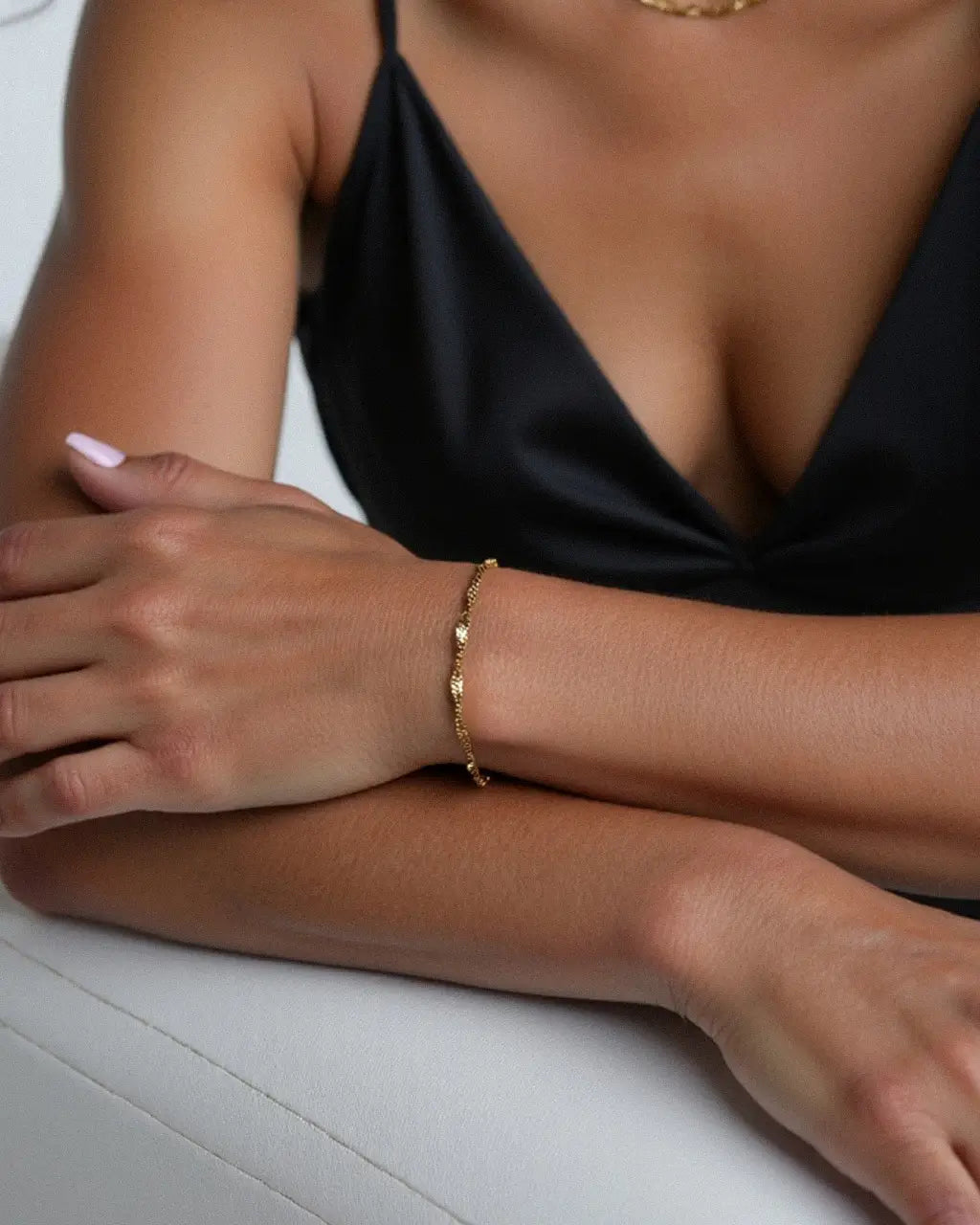 Anchor Twist Chain Bracelet – worn on the wrist, arm resting across the body, gold, black satin top