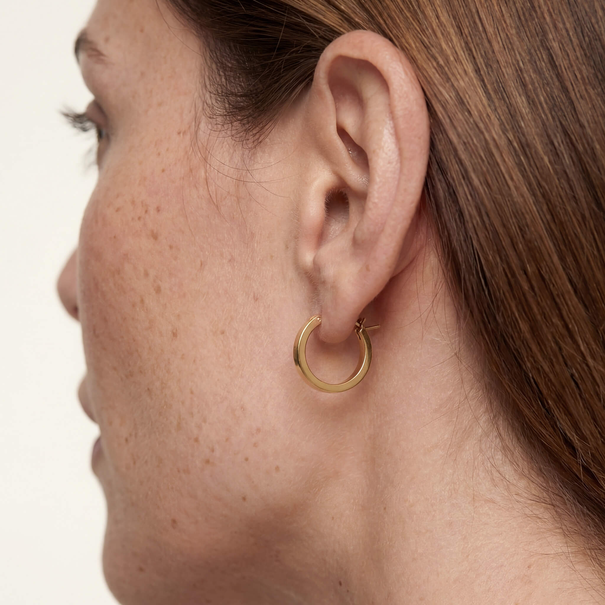Crossing Hoops gold hoop earring worn close up on a woman's ear