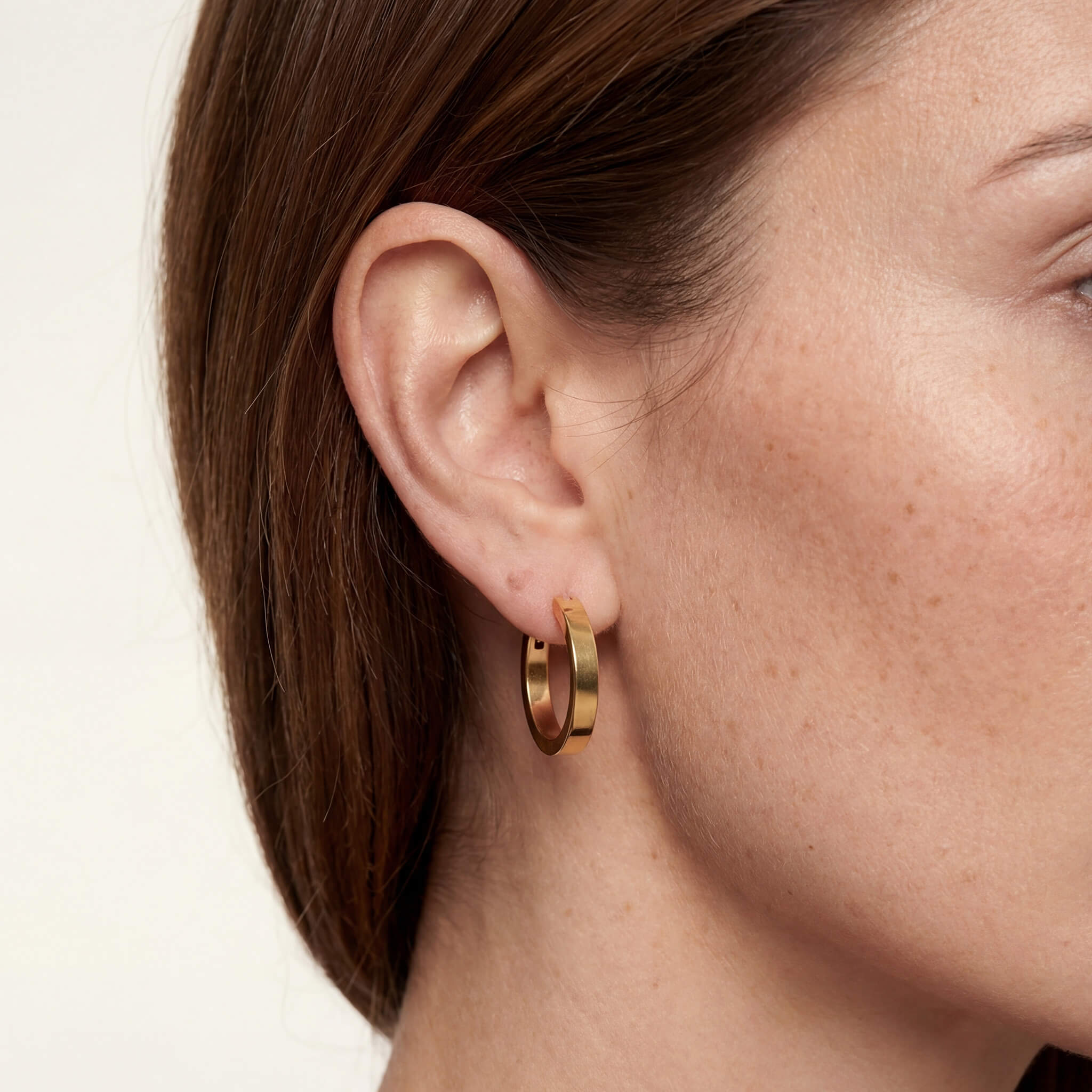 Crossing Hoops worn on a woman's ear, thick flat gold hoop earring close-up