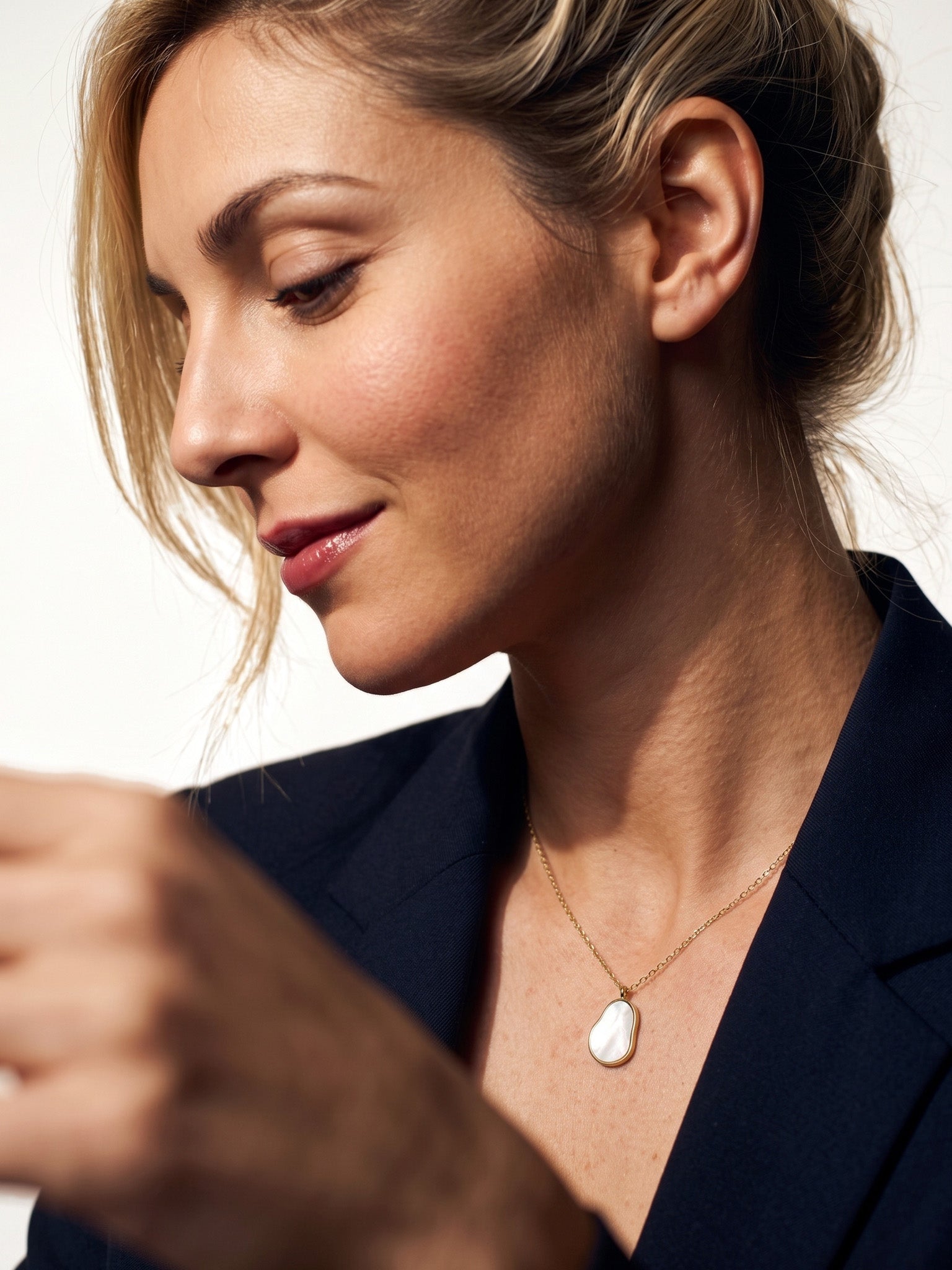 Dawn Pearl Pendant Necklace – side view, looking down, mother-of-pearl pendant on the chest, navy blazer, ivory studio background