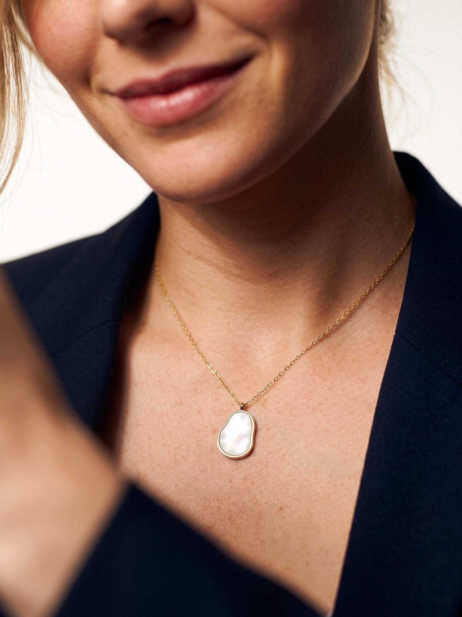 Dawn Pearl Pendant Necklace – close crop of a smile and the mother-of-pearl pendant, navy blazer, ivory studio background
