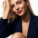 Dawn Pearl Pendant Necklace – worn on the chest, seated with a hand in her hair, navy blazer, mother-of-pearl pendant, ivory studio background