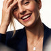 Dawn Pearl Pendant Necklace – worn on the chest, laughing with a hand on her forehead, navy blazer, mother-of-pearl pendant, ivory studio background
