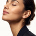 Evening Grace Drop Earrings – worn in the ear, head tilted back with eyes closed in side view, gold, dark blazer, hair in a low bun