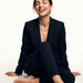 Everlasting Chain Necklace – worn at the collarbone, seated on the floor laughing, gold, black suit, ivory studio background