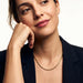 Everlasting Chain Necklace – worn at the collarbone, head resting on a fist, gold, black blazer, ivory studio background