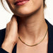 Everlasting Chain Necklace – close crop of a smile and the flat snake chain at the collarbone, hand at the neck, gold, black blazer, ivory studio background