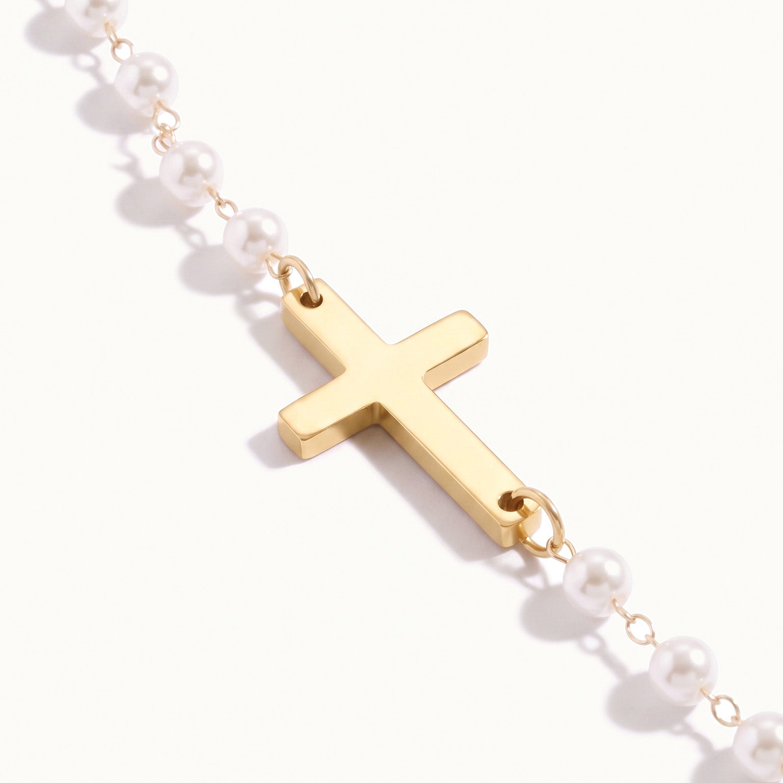 Every Season Cross Necklace – close-up of the gold cross between the pearls, on ivory background