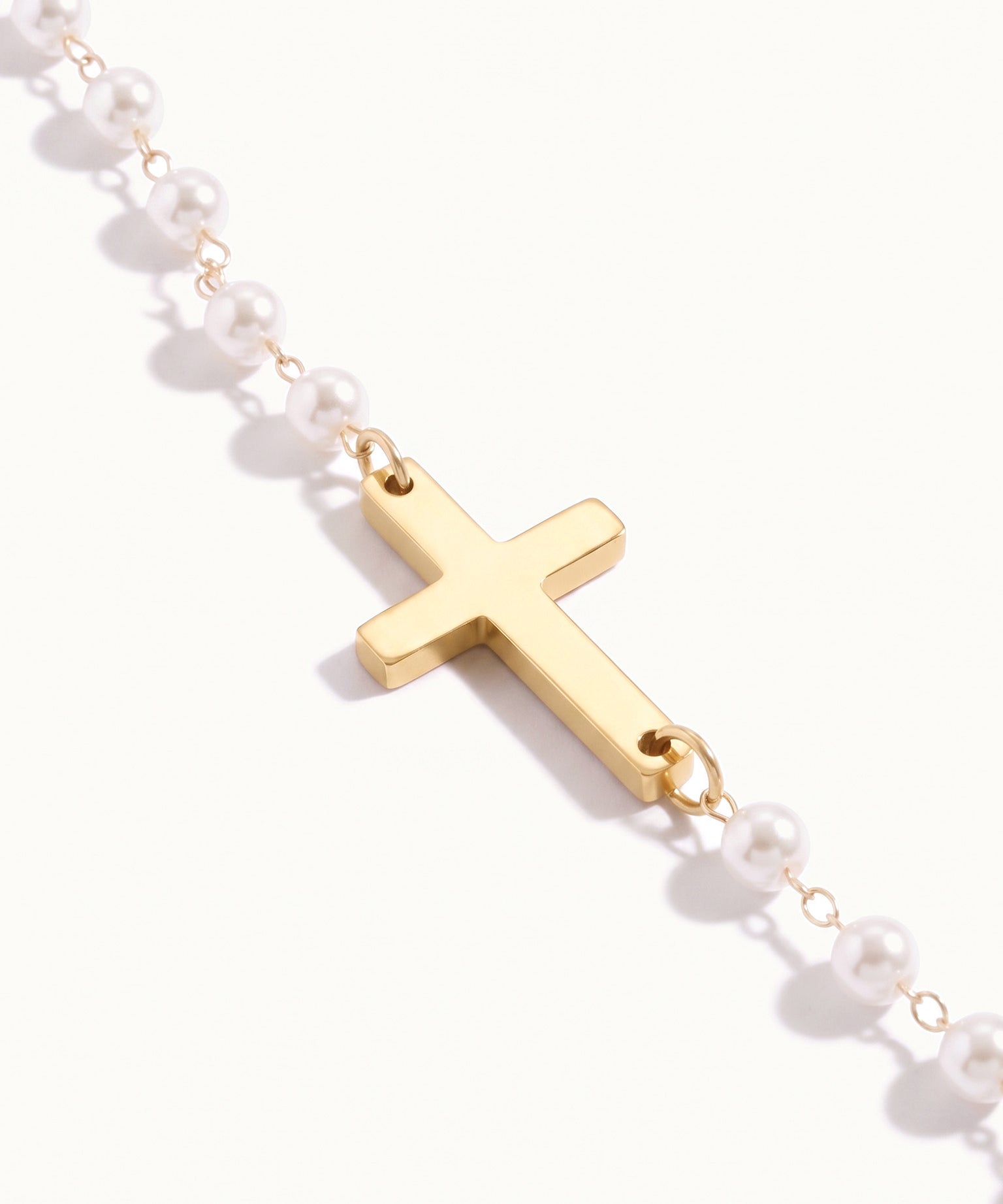 Every Season Cross Necklace – close-up of the gold cross between the pearls, on ivory background