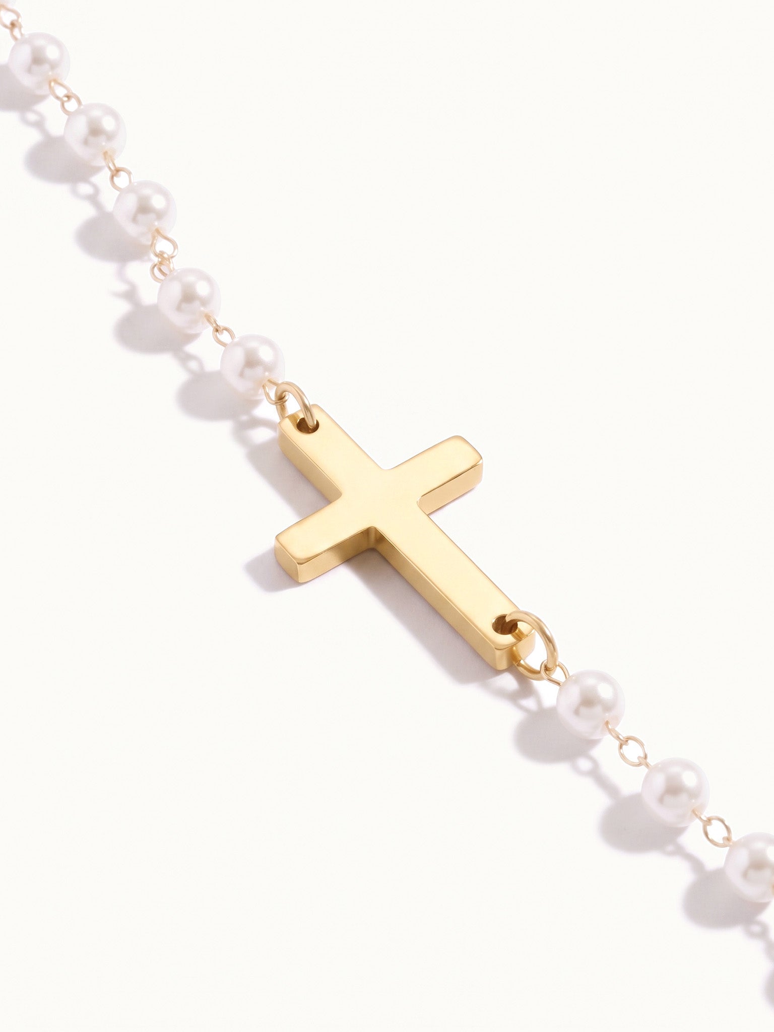 Every Season Cross Necklace – close-up of the gold cross between the pearls, on ivory background