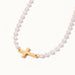 Every Season Cross Necklace – gold cross on a strand of tiny pearls, hanging in a curve, on ivory background