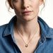 Everyday Loop Necklace – gold loop pendant on a fine chain at the collarbone, model with red hair in a blue denim shirt, ivory studio background