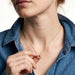 Everyday Loop Necklace – fingers holding the gold loop pendant on its fine chain, blue denim shirt, ivory studio background