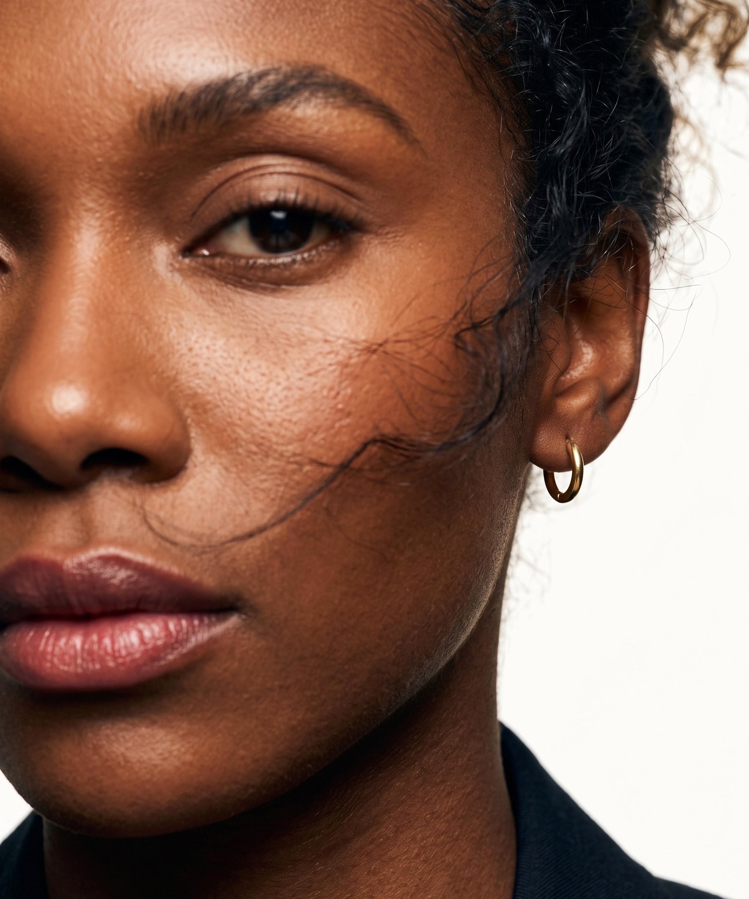 Faithful Hoops – worn in the ear, close crop of the face with loose hair across the cheek, gold hoop, curly hair up