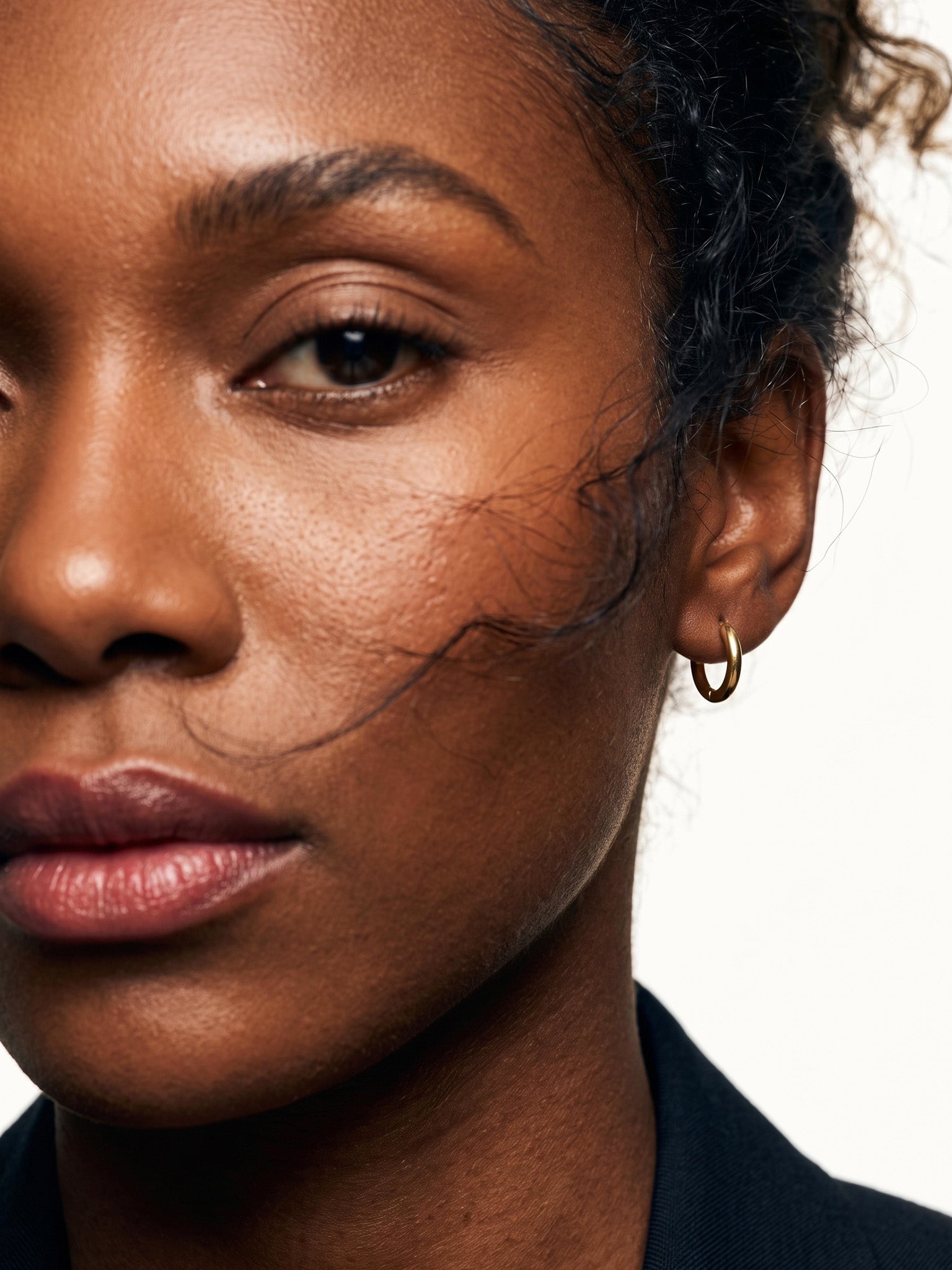 Faithful Hoops – worn in the ear, close crop of the face with loose hair across the cheek, gold hoop, curly hair up
