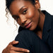 Faithful Hoops – worn in the ear, head tilted with a soft smile and an arm around the knee, gold hoop, curly hair up