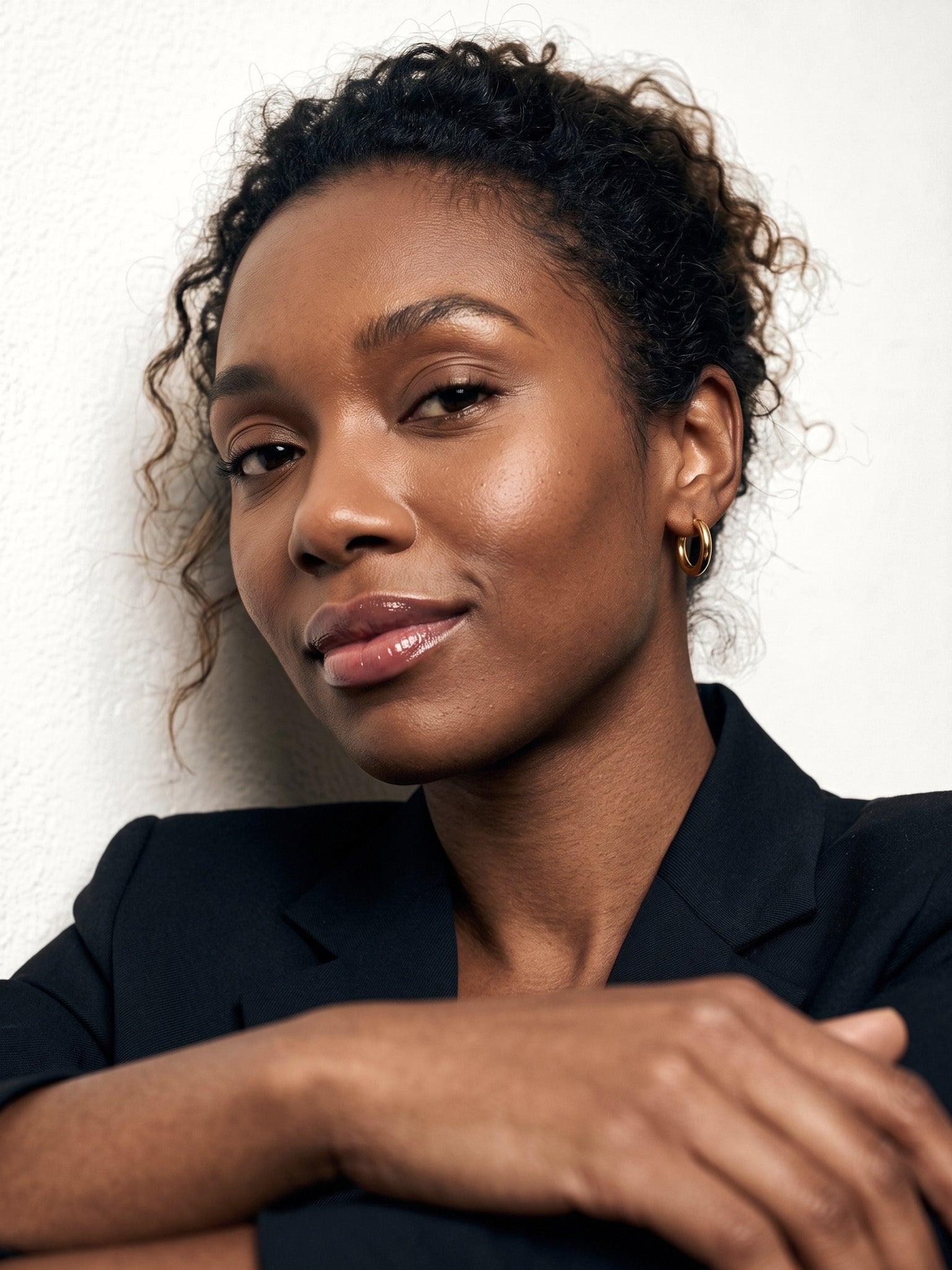Faithful Hoops – worn in the ear, leaning against a wall with arms folded, gold hoop, curly hair up