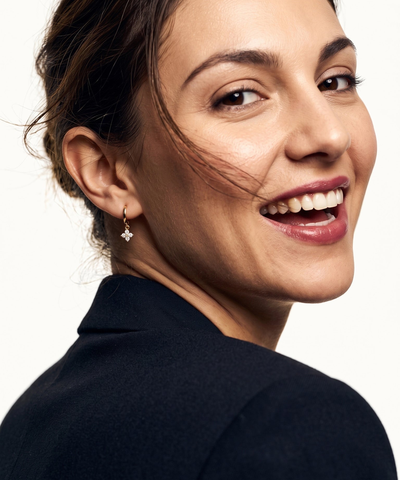 Field Lily Drop Earrings – worn in the ear, laughing and looking back over the shoulder, gold huggie with a four-stone flower drop, dark hair up