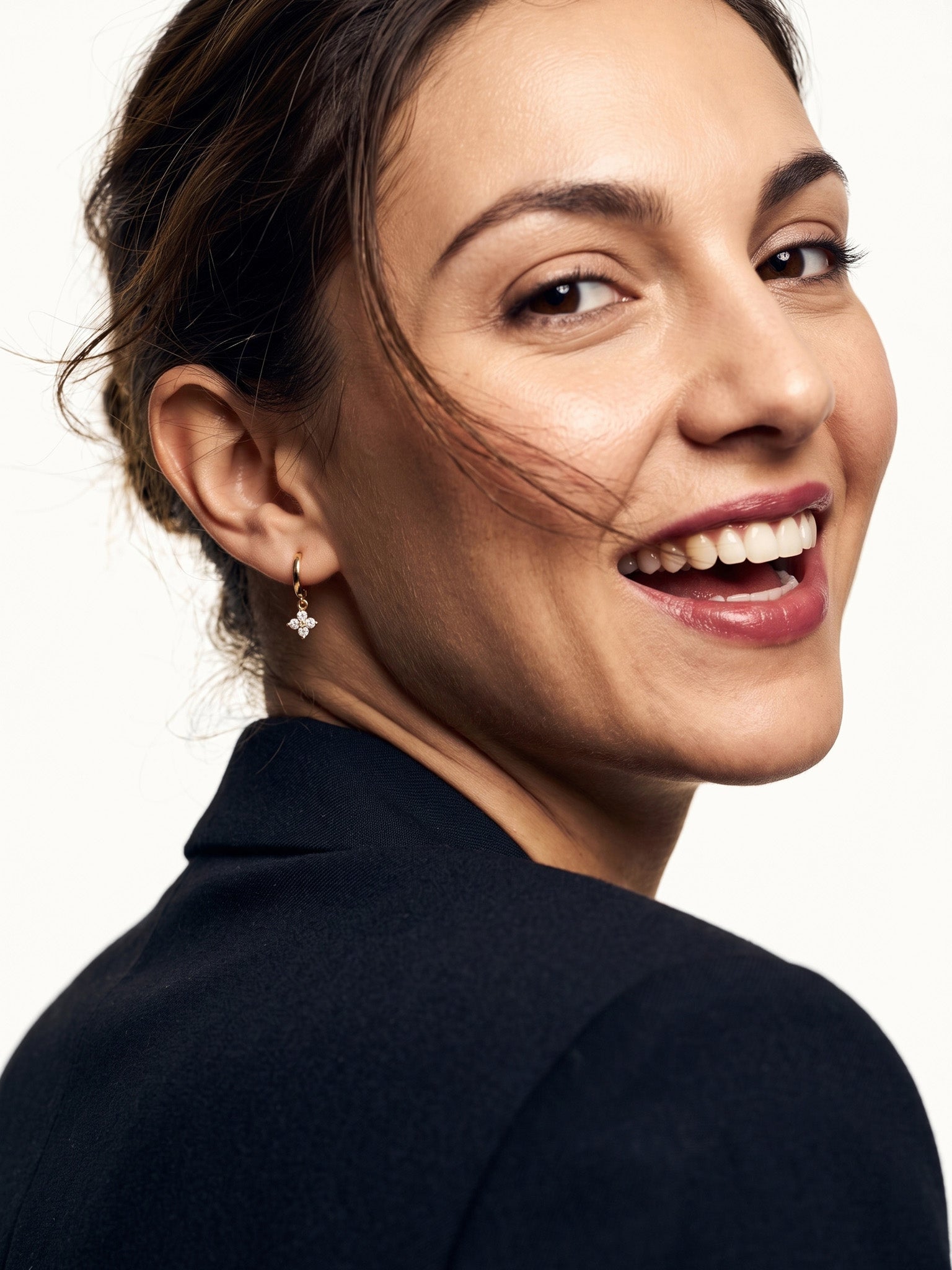 Field Lily Drop Earrings – worn in the ear, laughing and looking back over the shoulder, gold huggie with a four-stone flower drop, dark hair up