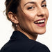 Field Lily Drop Earrings – worn in the ear, laughing and looking back over the shoulder, gold huggie with a four-stone flower drop, dark hair up