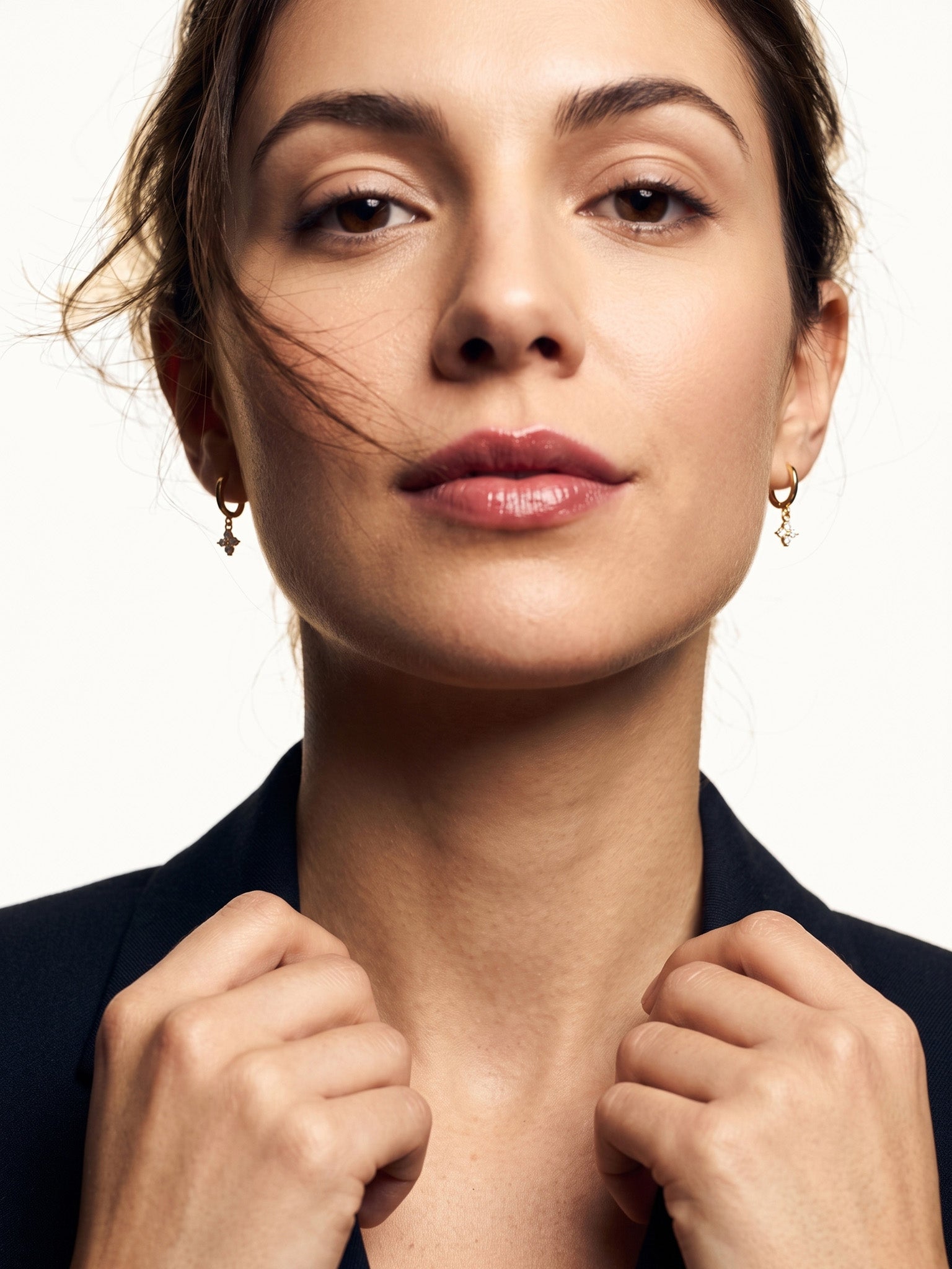 Field Lily Drop Earrings – worn in both ears, facing the camera with hands at the collar, gold huggies with four-stone flower drops, dark hair up
