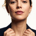 Field Lily Drop Earrings – worn in both ears, facing the camera with hands at the collar, gold huggies with four-stone flower drops, dark hair up