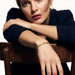 Fire & Roots Cuff – worn on the wrist, arm resting over the back of a wooden chair, gold, dark blazer, ivory studio background