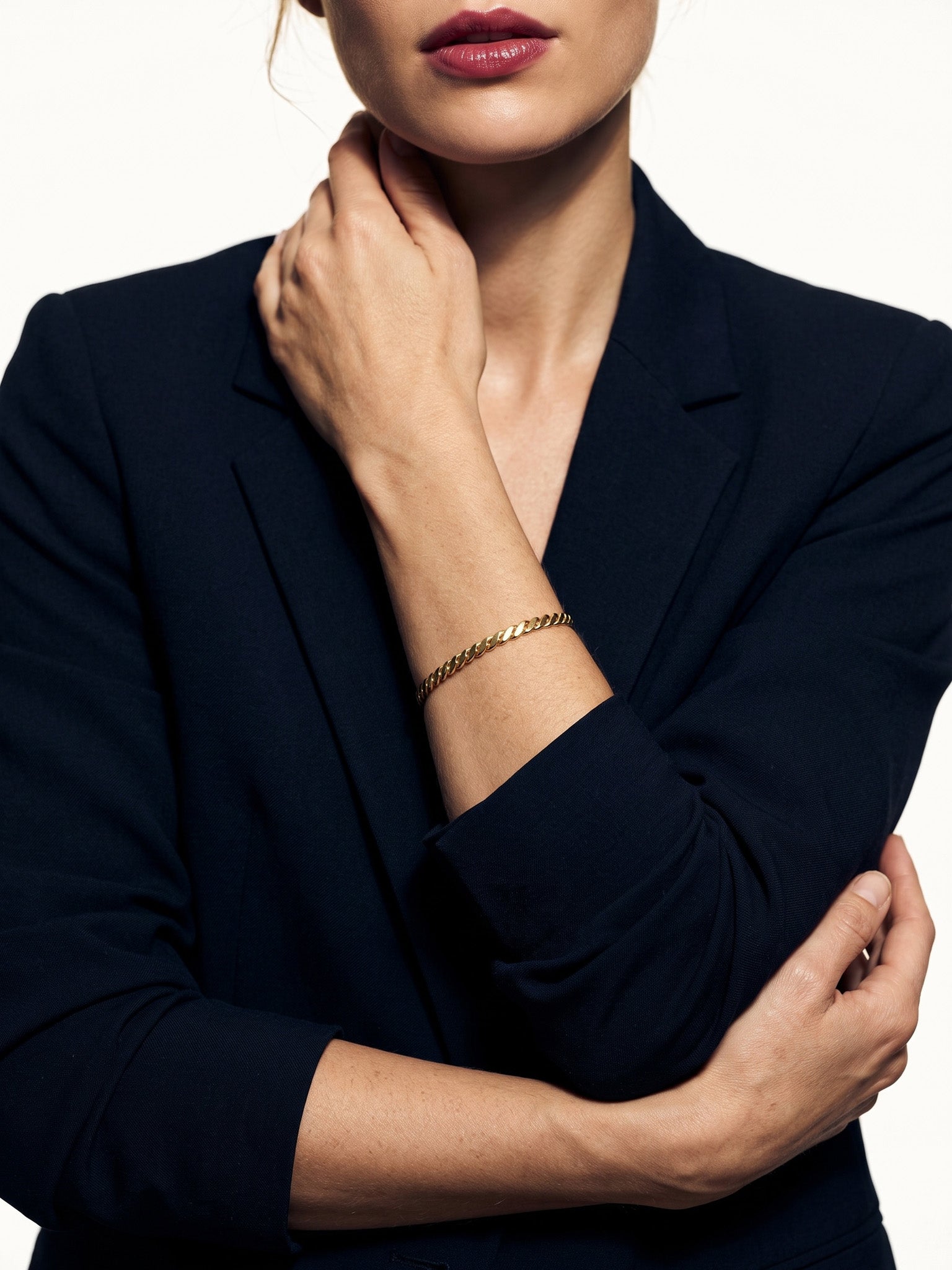 Fire & Roots Cuff – worn on the wrist, hand raised to the neck, gold, dark blazer, ivory studio background