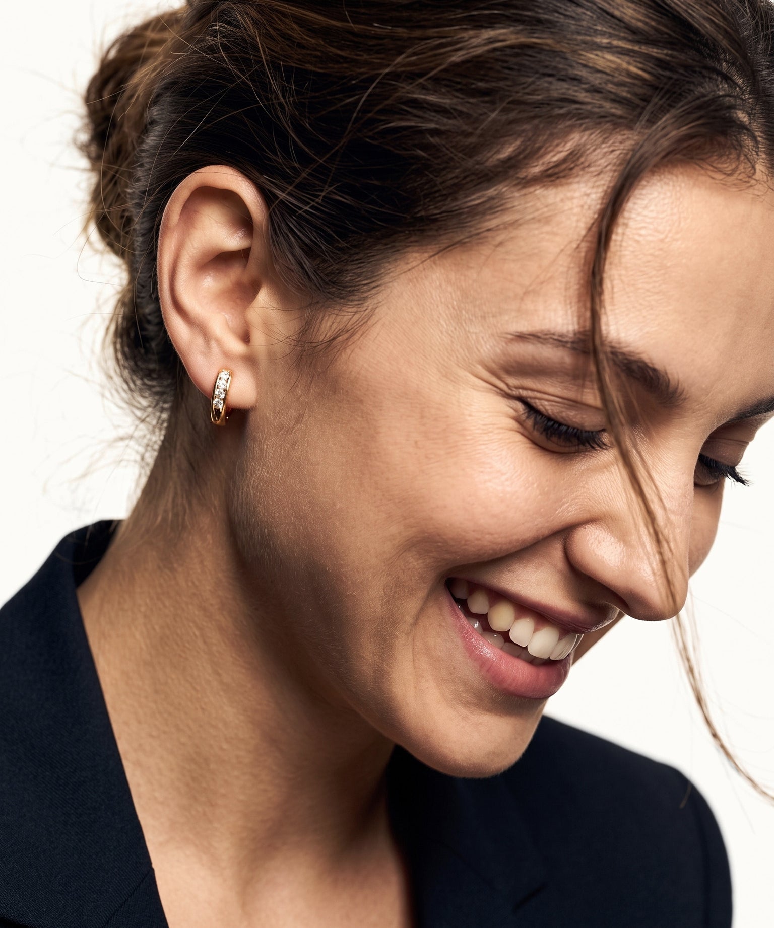 Four Seasons Huggies – worn in the ear, laughing and looking down with hair in motion, gold four-stone huggie, dark hair up