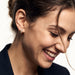 Four Seasons Huggies – worn in the ear, laughing and looking down with hair in motion, gold four-stone huggie, dark hair up