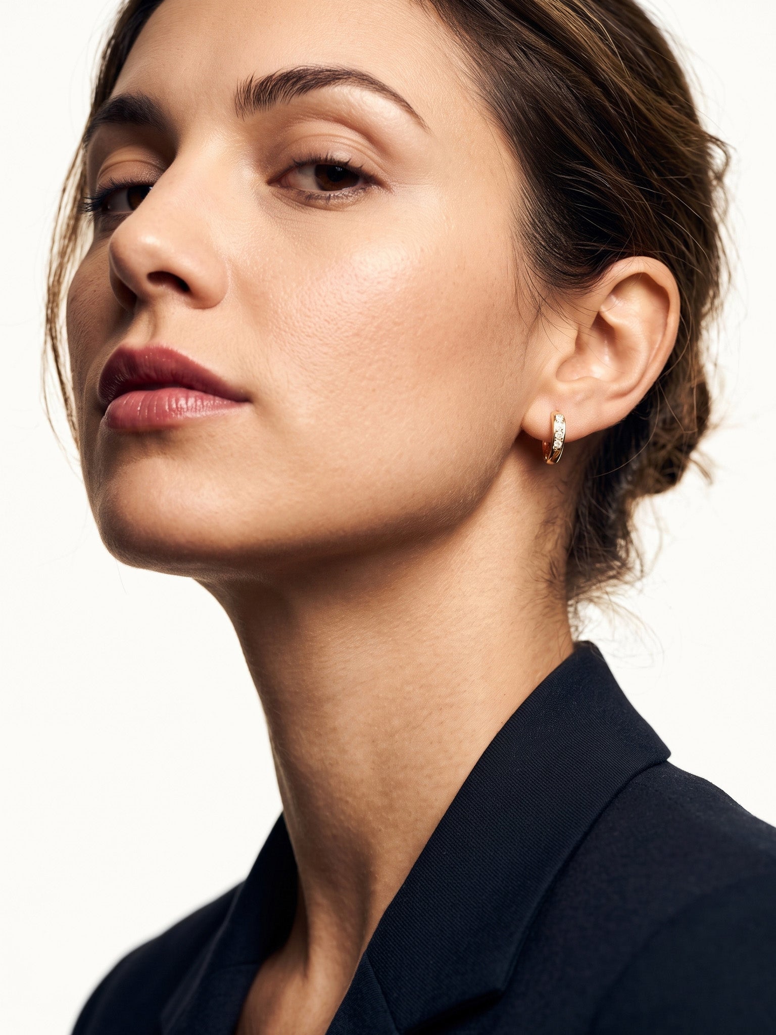 Four Seasons Huggies – worn in the ear, head tilted back with chin lifted, gold four-stone huggie, dark hair up