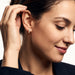 Four Seasons Huggies – worn in the ear, hand in the hair, looking down with a soft smile, gold four-stone huggie, dark hair up