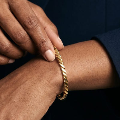 Hands adjusting a gold curb bangle on the wrist, black blazer