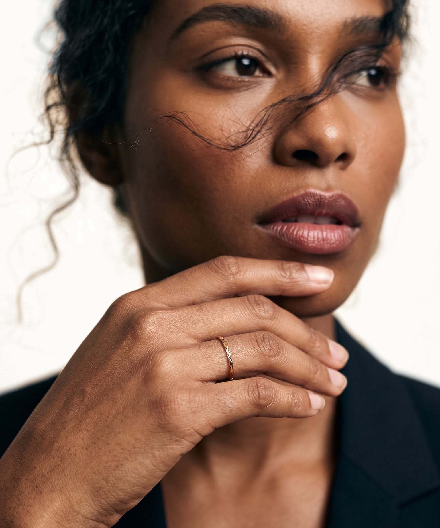 Golden Season Band Ring – worn with fingertips at the chin, gold, dark blazer, ivory studio background