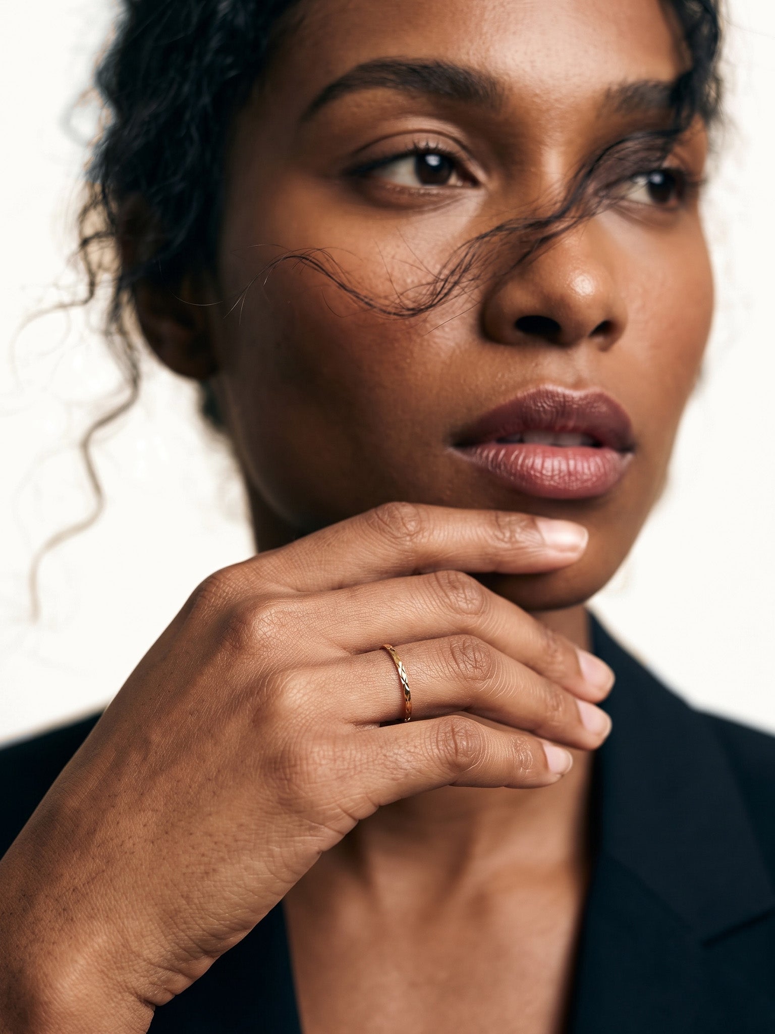 Golden Season Band – worn with fingertips at the chin, gold, dark blazer, ivory studio background