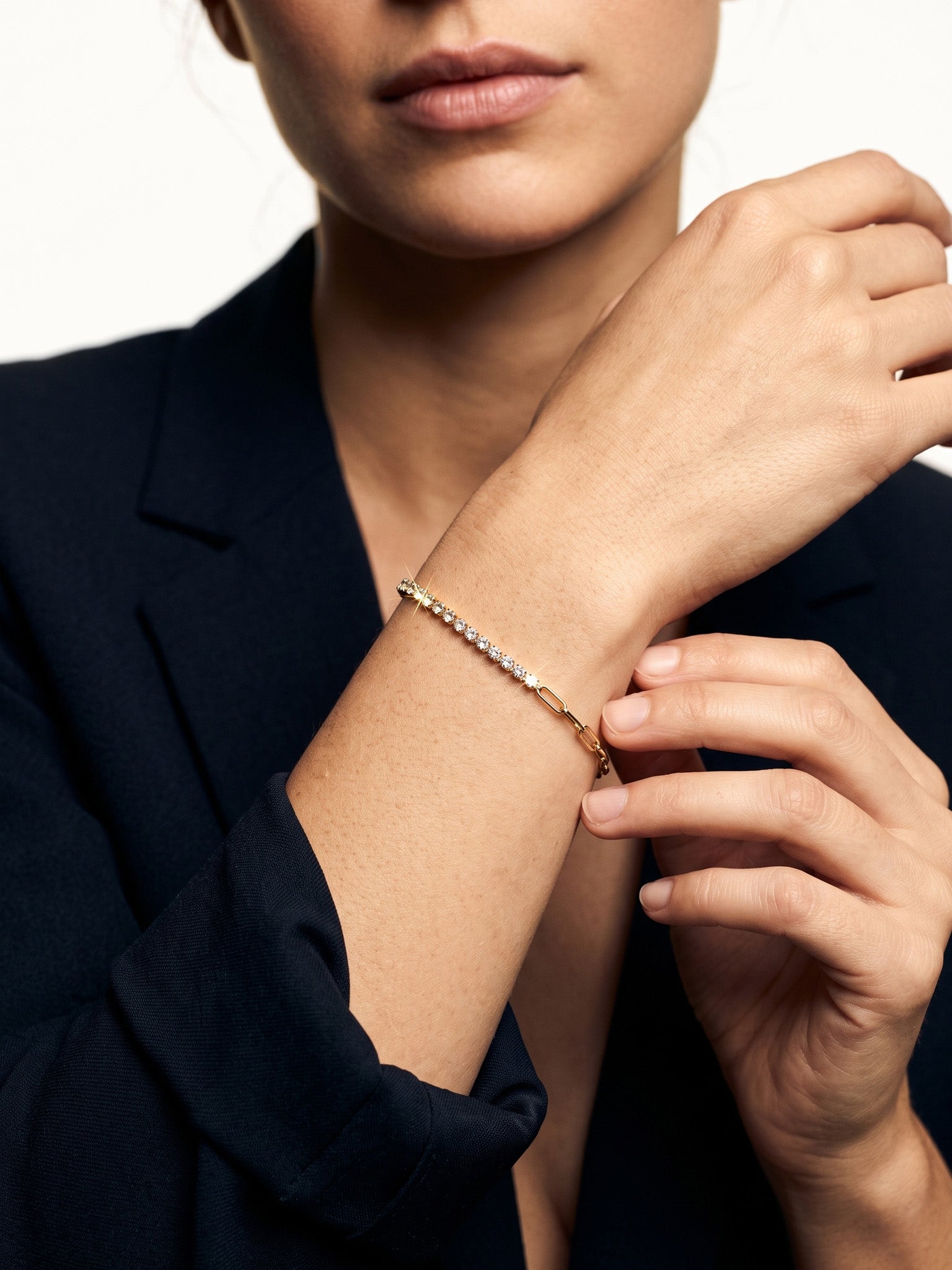 Grace Line Bracelet – worn on the wrist, one hand adjusting the bracelet, gold, dark blazer, ivory studio background