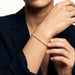 Grace Line Bracelet – worn on the wrist, one hand adjusting the bracelet, gold, dark blazer, ivory studio background
