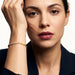 Grace Line Bracelet – worn on the wrist, hand raised to the forehead, gold, dark blazer, ivory studio background