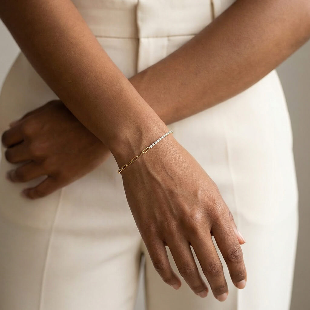 Grace Line Bracelet – worn on the wrist with arms crossed, gold, cream trousers