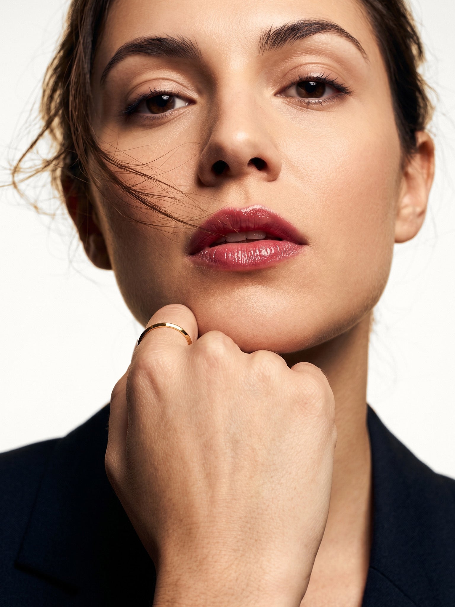 Grace Stack Ring – worn on a closed hand beneath the chin, gold, dark blazer, ivory studio background
