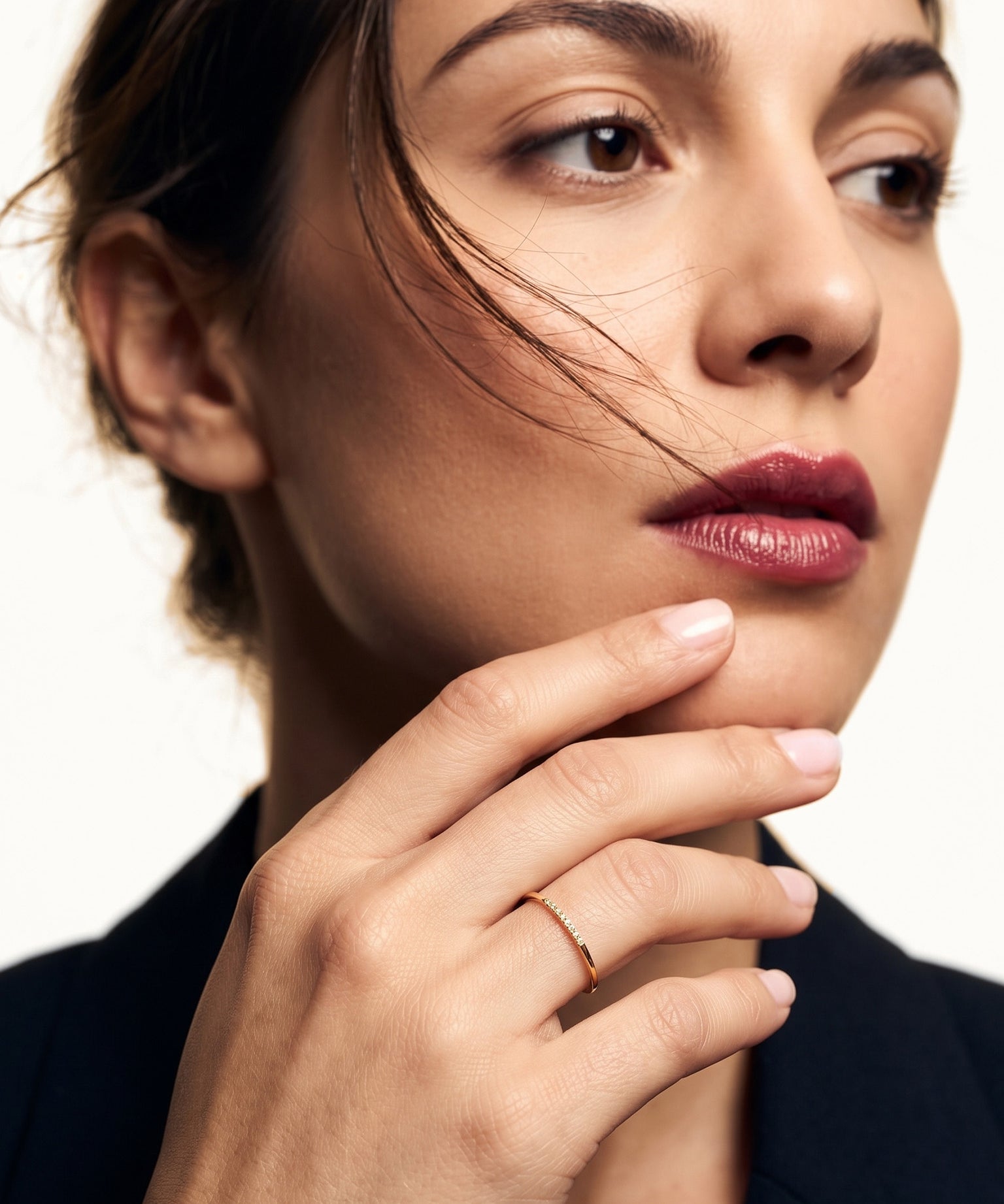 Halo Band Ring – worn with the fingers resting at the chin, gold, dark blazer, ivory studio background