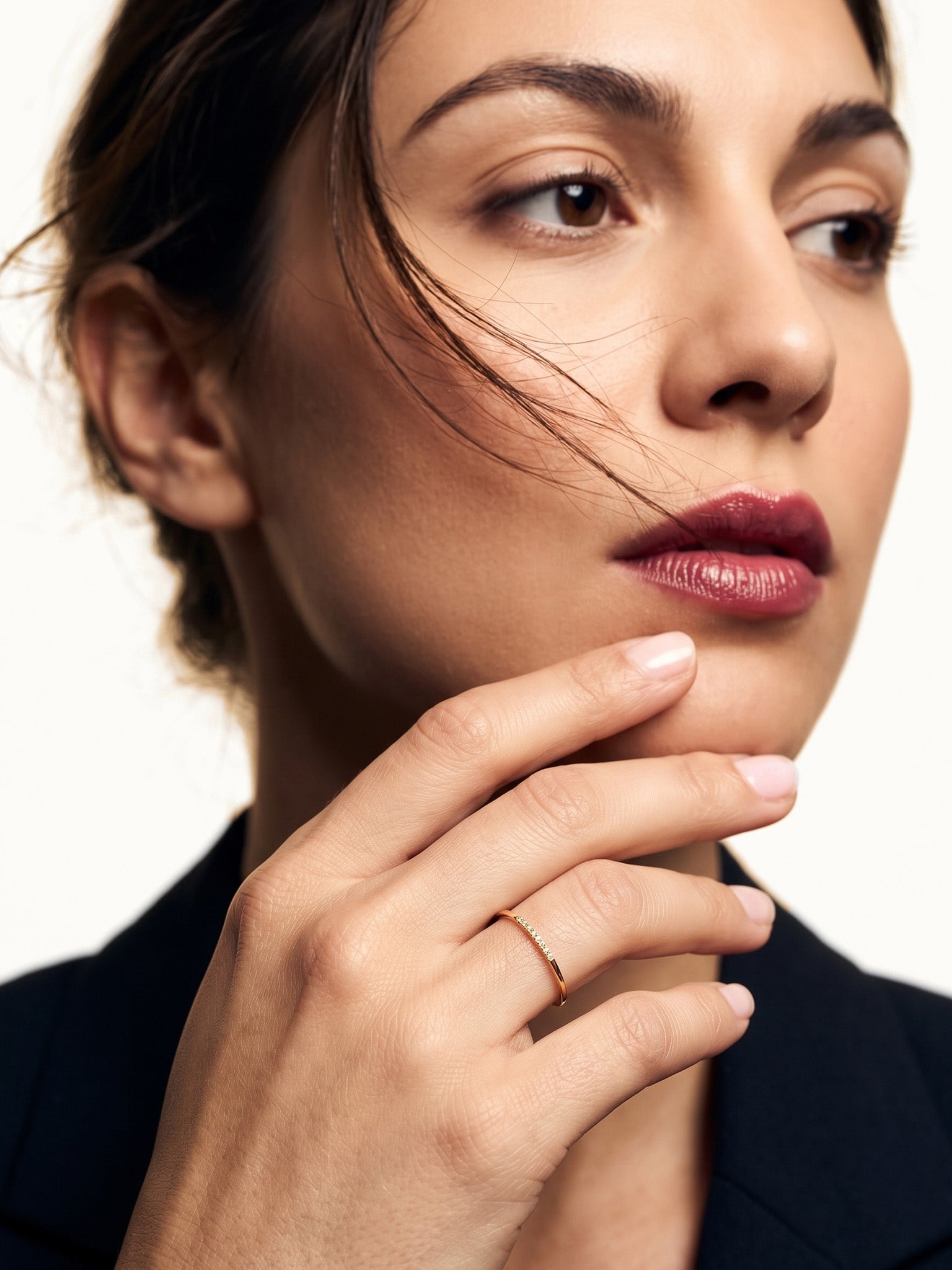 Halo Band Ring – worn with the fingers resting at the chin, gold, dark blazer, ivory studio background
