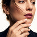 Halo Band Ring – worn with the fingers resting at the chin, gold, dark blazer, ivory studio background