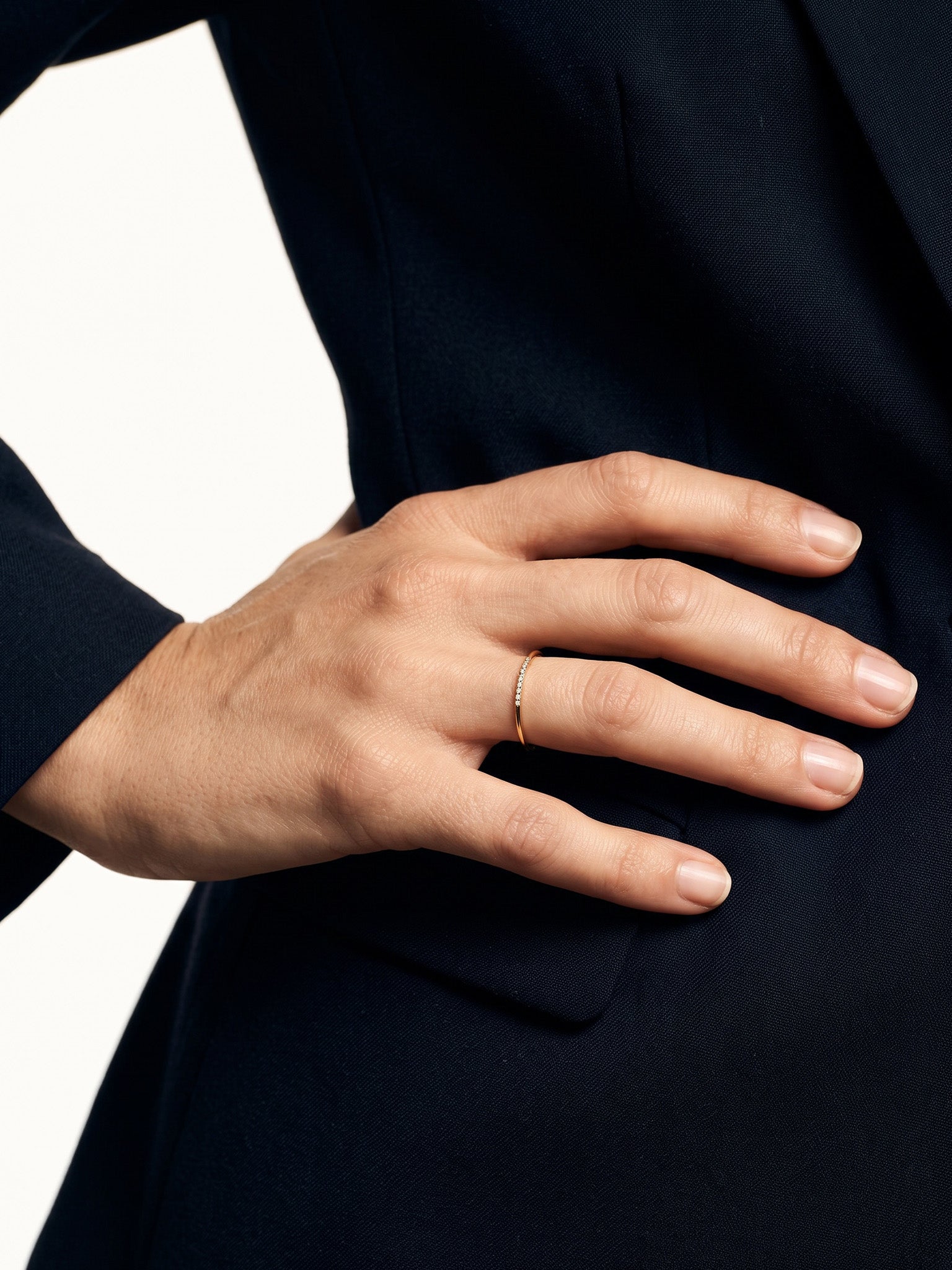 Halo Band Ring – worn with the hand resting on the hip, close-up, gold, dark blazer, ivory studio background