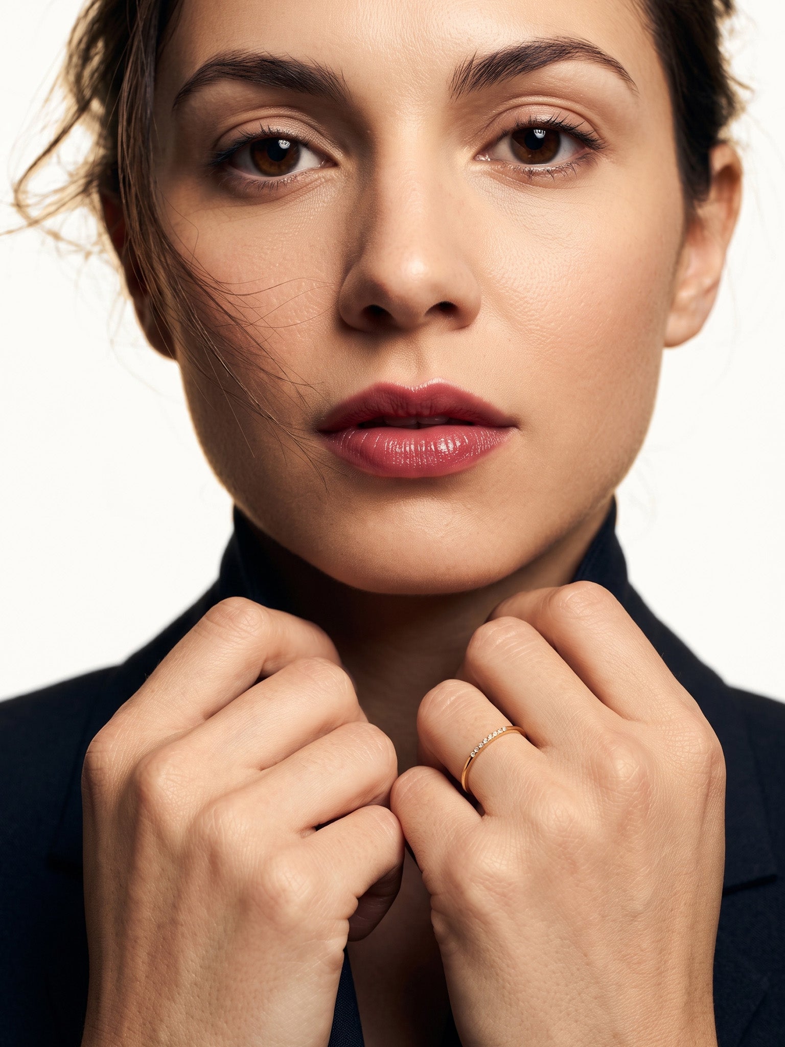 Halo Band Ring – worn with both hands holding the blazer collar, gold, dark blazer, ivory studio background