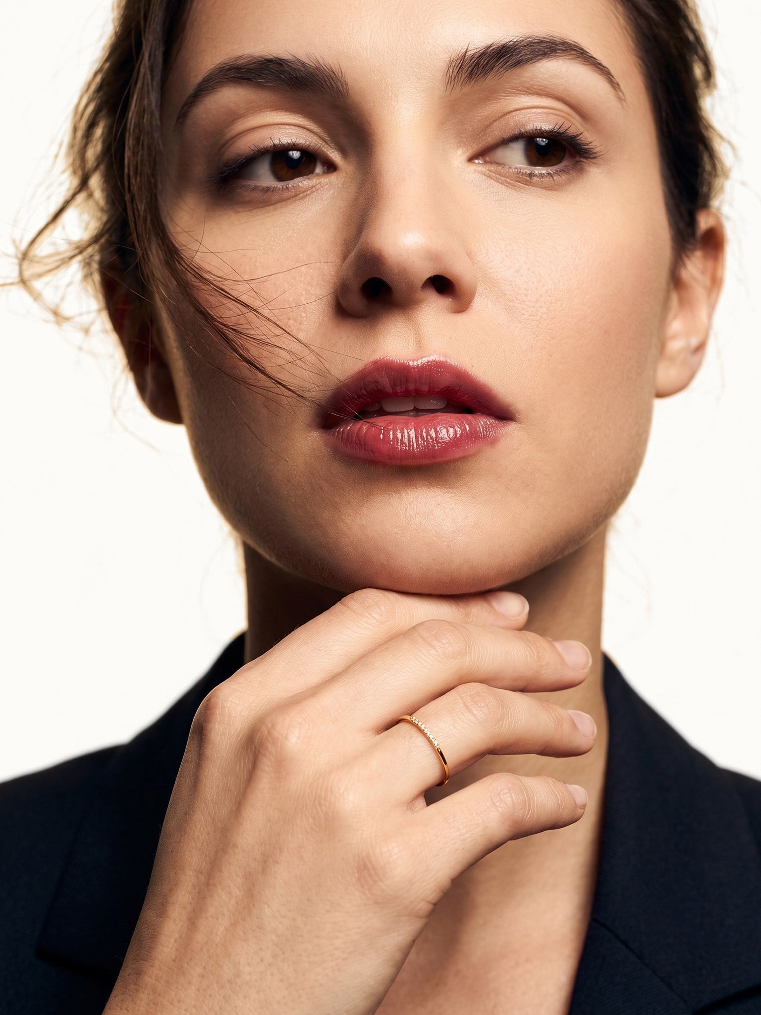 Halo Band Ring – worn on a hand resting beneath the chin, gold, dark blazer, ivory studio background