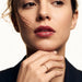 Halo Band Ring – worn on a hand resting beneath the chin, gold, dark blazer, ivory studio background